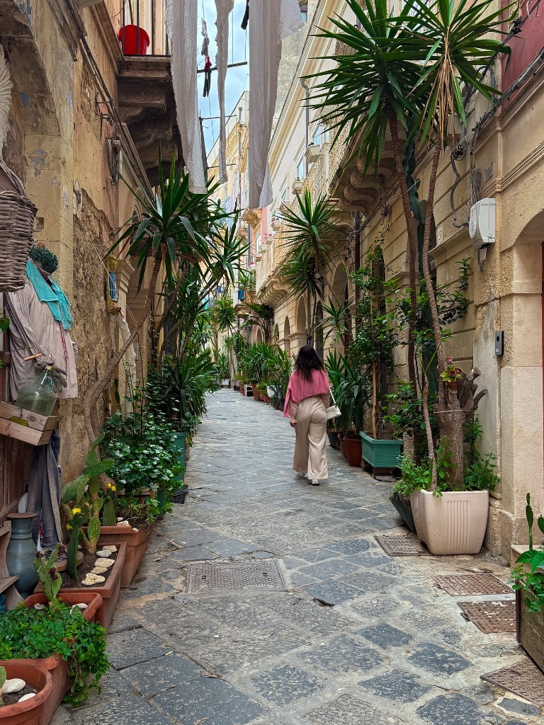 Mira walking down a cozy, plant-lined narrow stone street